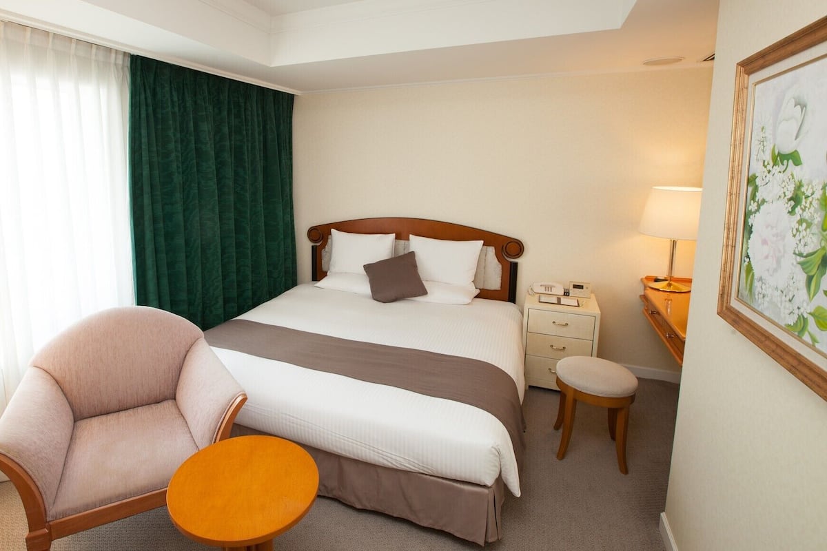 Ein Hotelzimmer mit Bett, Stuhl, kleinem Tisch, Nachttisch und Lampe.