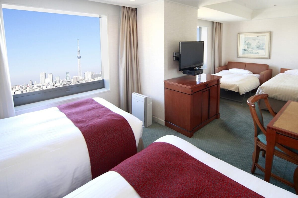 Ein Hotelzimmer mit zwei Betten, einem Schreibtisch, einem Fernseher und Blick auf die Stadt.