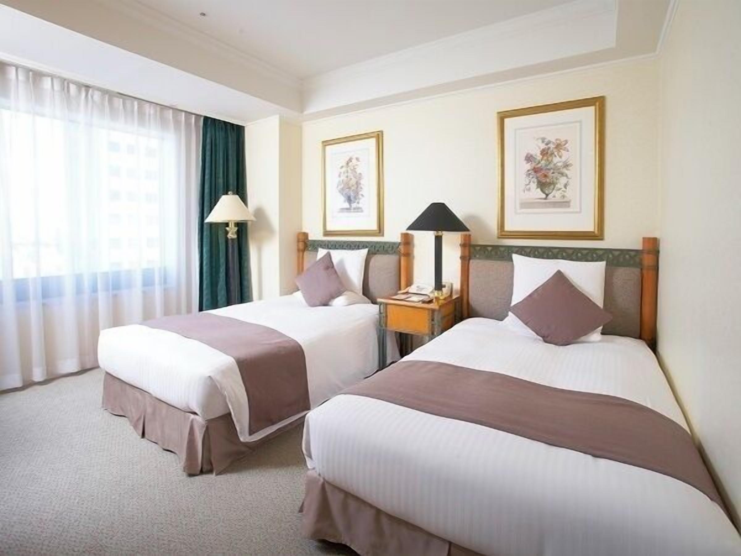 A hotel room with two beds, a nightstand, a lamp, and framed artwork on the wall.