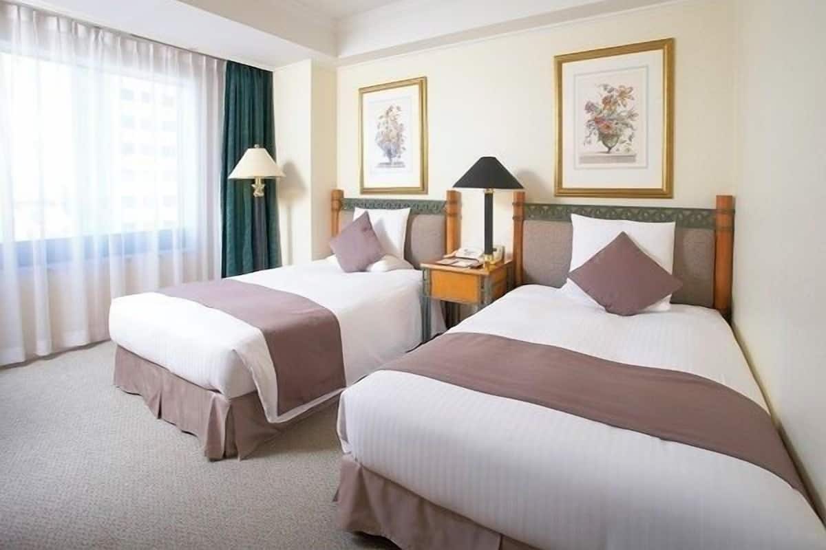 Ein Hotelzimmer mit zwei Betten, einem Nachttisch, einer Lampe und gerahmten Kunstwerken an der Wand.