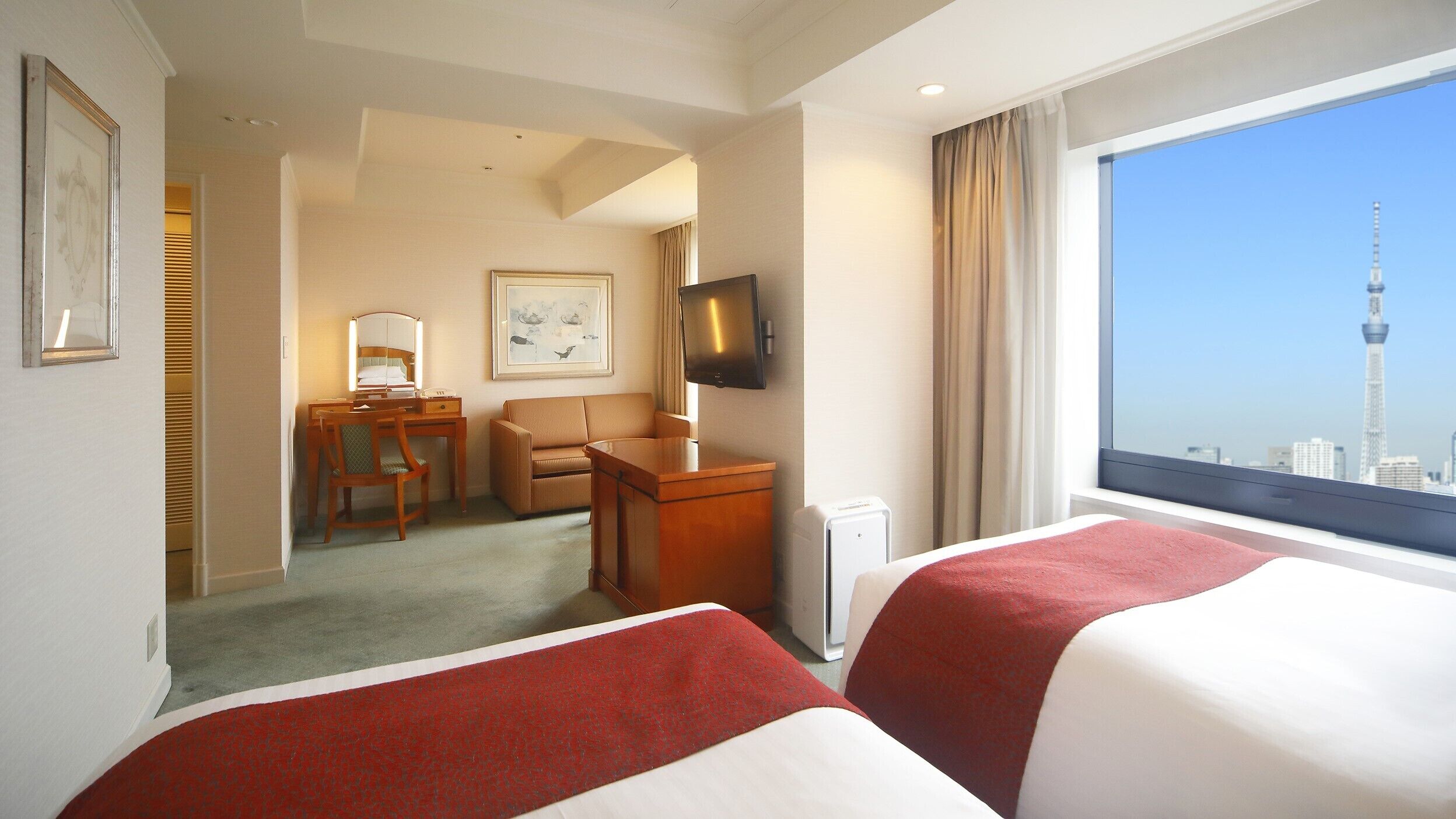 A hotel room with two beds, a desk with a chair, a television, and a window with a cityscape view.