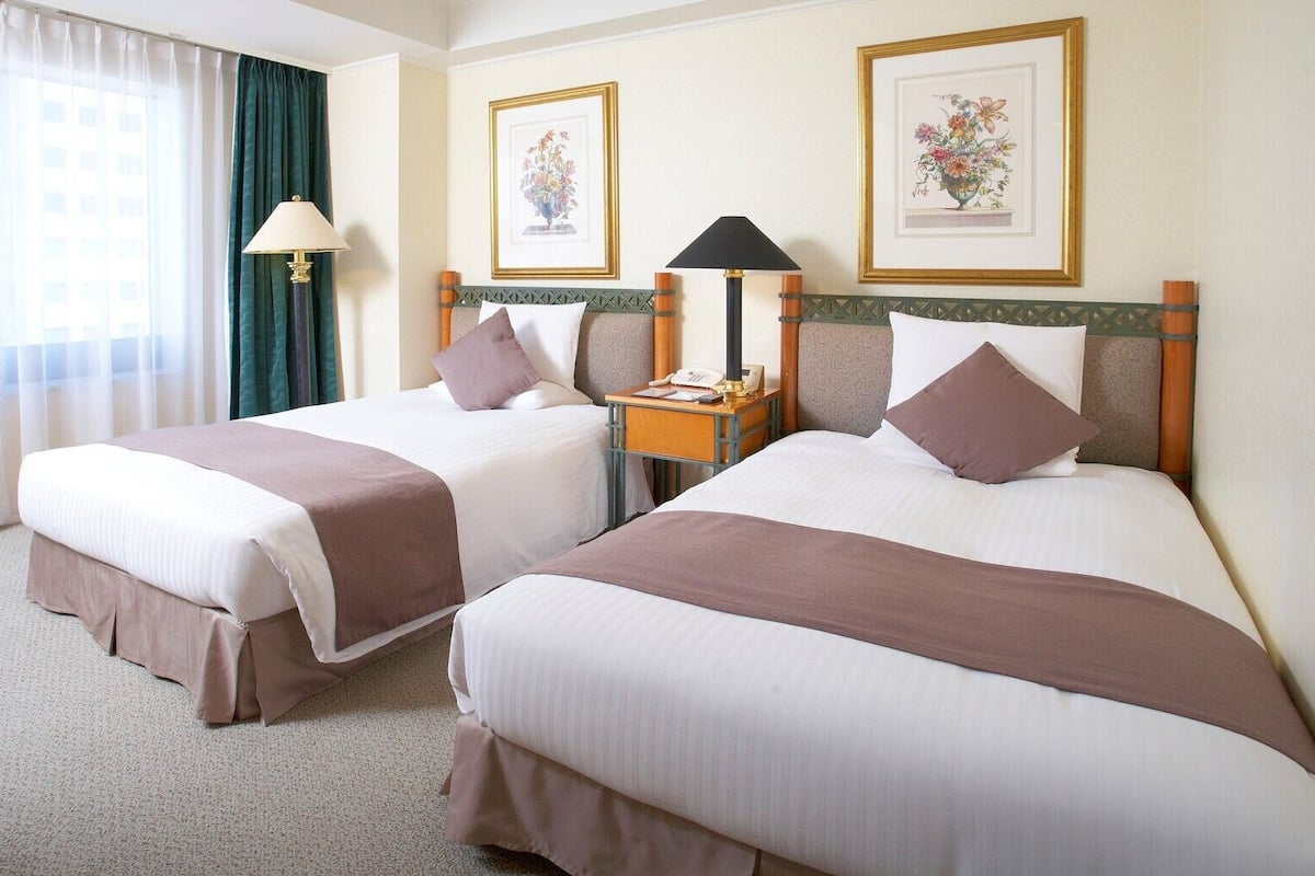 Ein Hotelzimmer mit zwei Betten, einem Nachttisch, einer Lampe und gerahmten Blumenbildern an den Wänden.