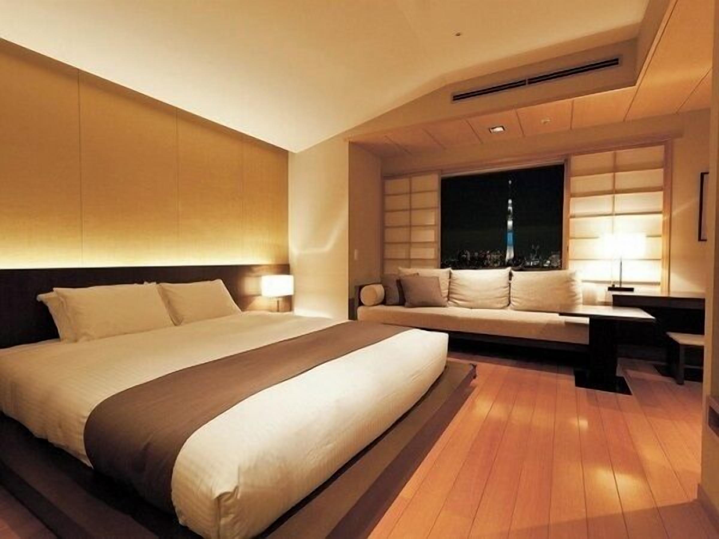 A modern hotel room with a large bed, a sofa, a desk, and a window with a city view.