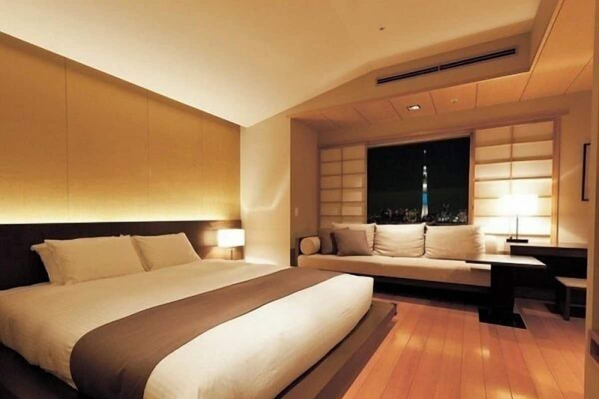 Ein modernes Hotelzimmer mit einem großen Bett, einer Couch, einem Schreibtisch und einem Fenster mit Blick auf die Stadt.