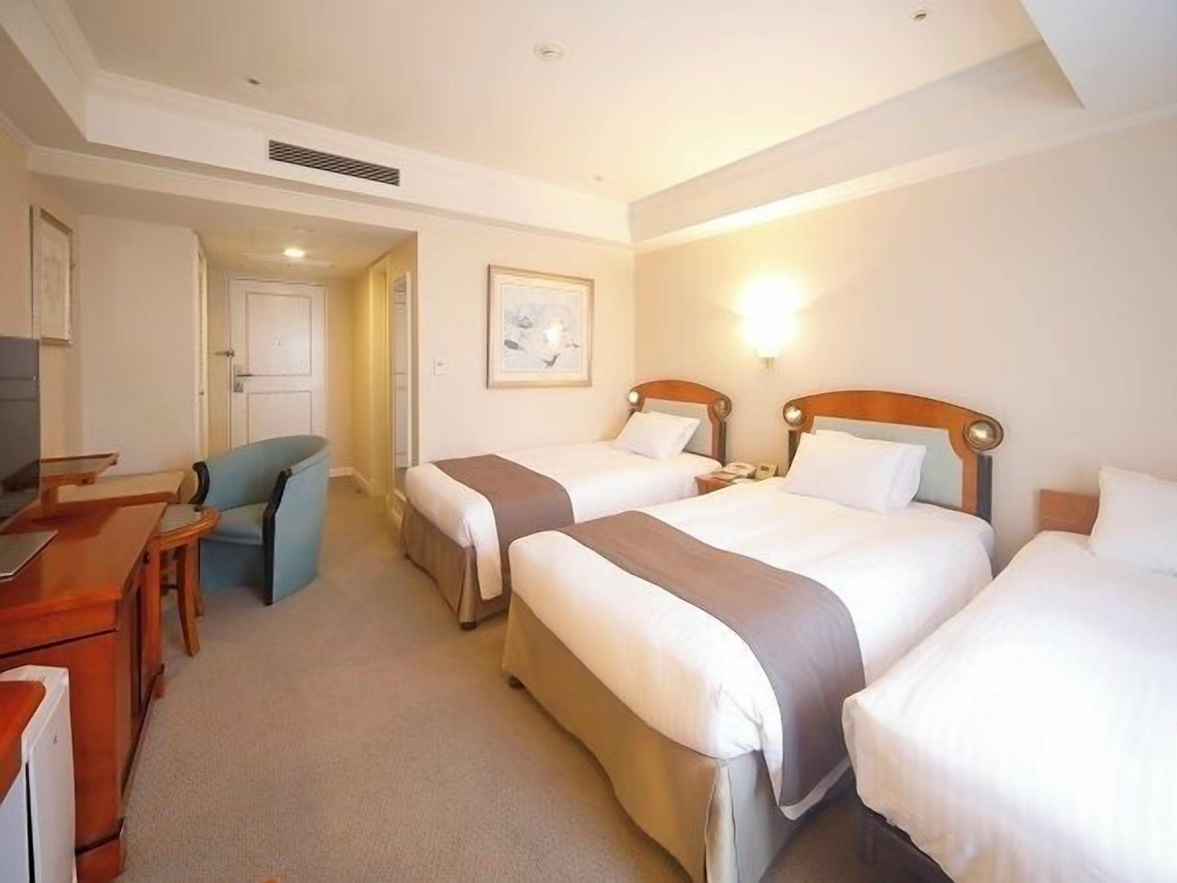 A hotel room with two beds, a desk, a chair, and a television.