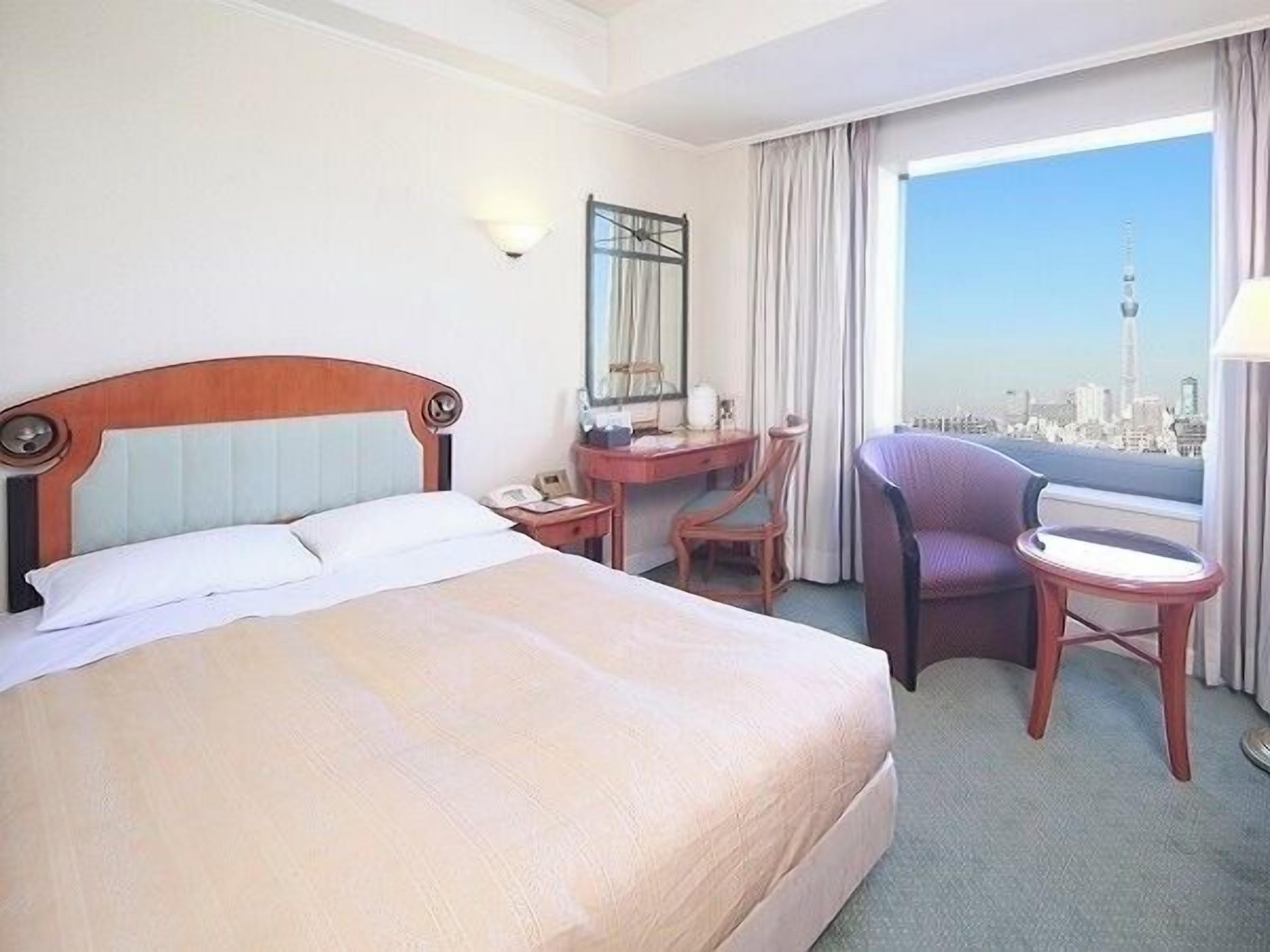 A hotel room with a bed, desk, chair, and a view of a cityscape.