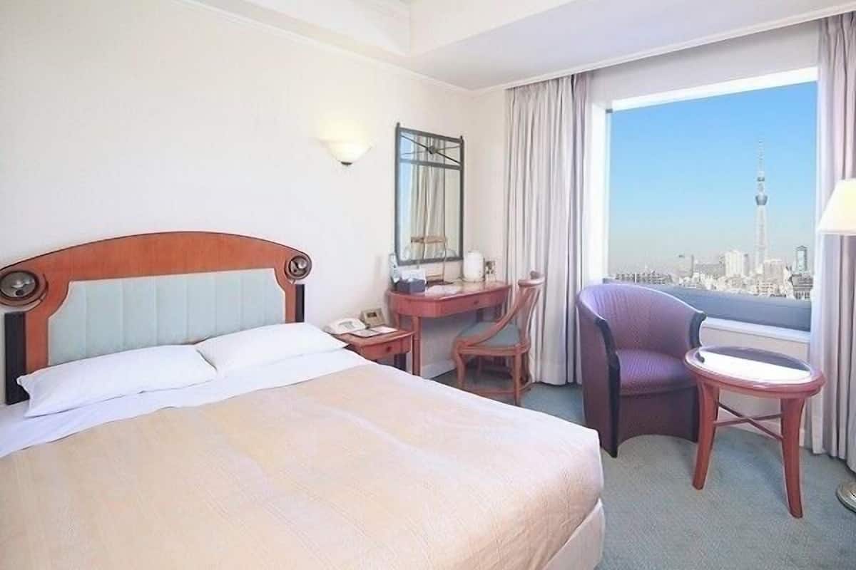 Ein Hotelzimmer mit Bett, Schreibtisch, Stuhl und Blick auf eine Stadtlandschaft.