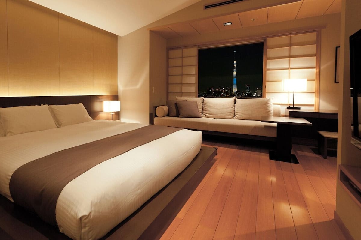 Ein Hotelzimmer mit einem großen Bett, einer Couch, einem Nachttisch und einem Fenster mit Blick auf die Stadt.