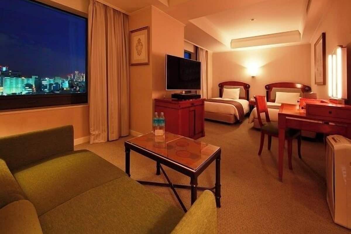 Ein Hotelzimmer mit Bett, Schreibtisch, Fernseher, Fenster mit Stadtblick und einem Sessel.