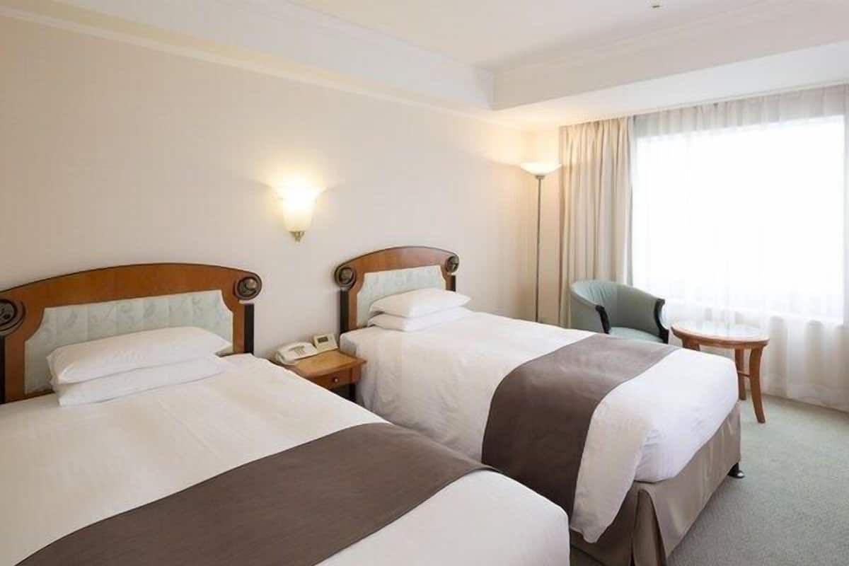 Ein Hotelzimmer mit zwei Betten, einem Sessel, einem kleinen Tisch und einer Lampe.