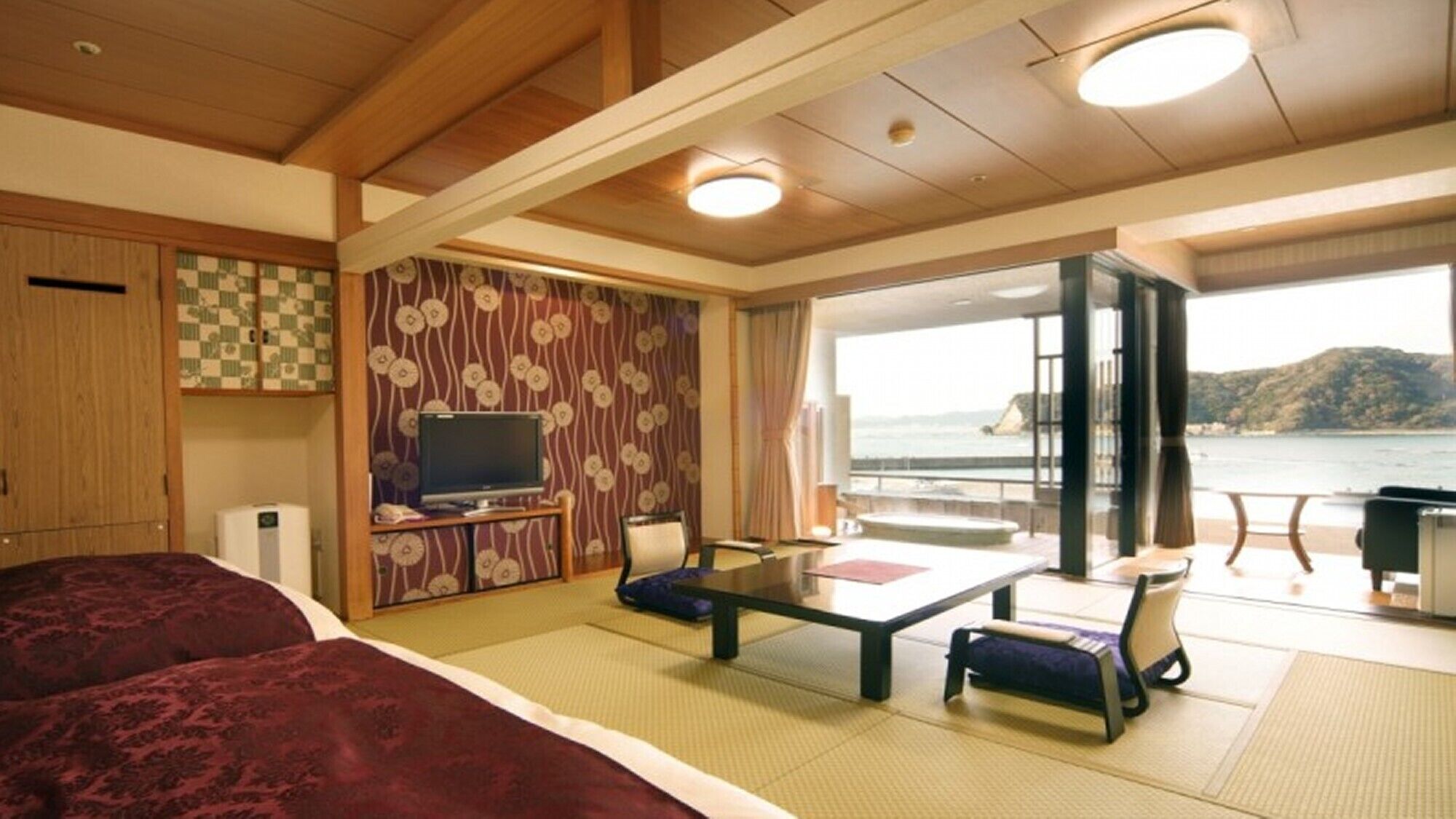 A room with a bed, a TV, a dining table, and a view of the sea.