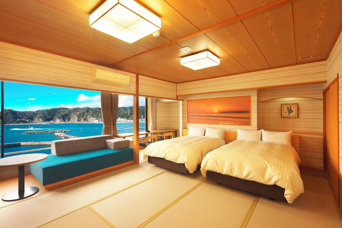 A room with two beds, a sofa, a table, and a view of the sea.