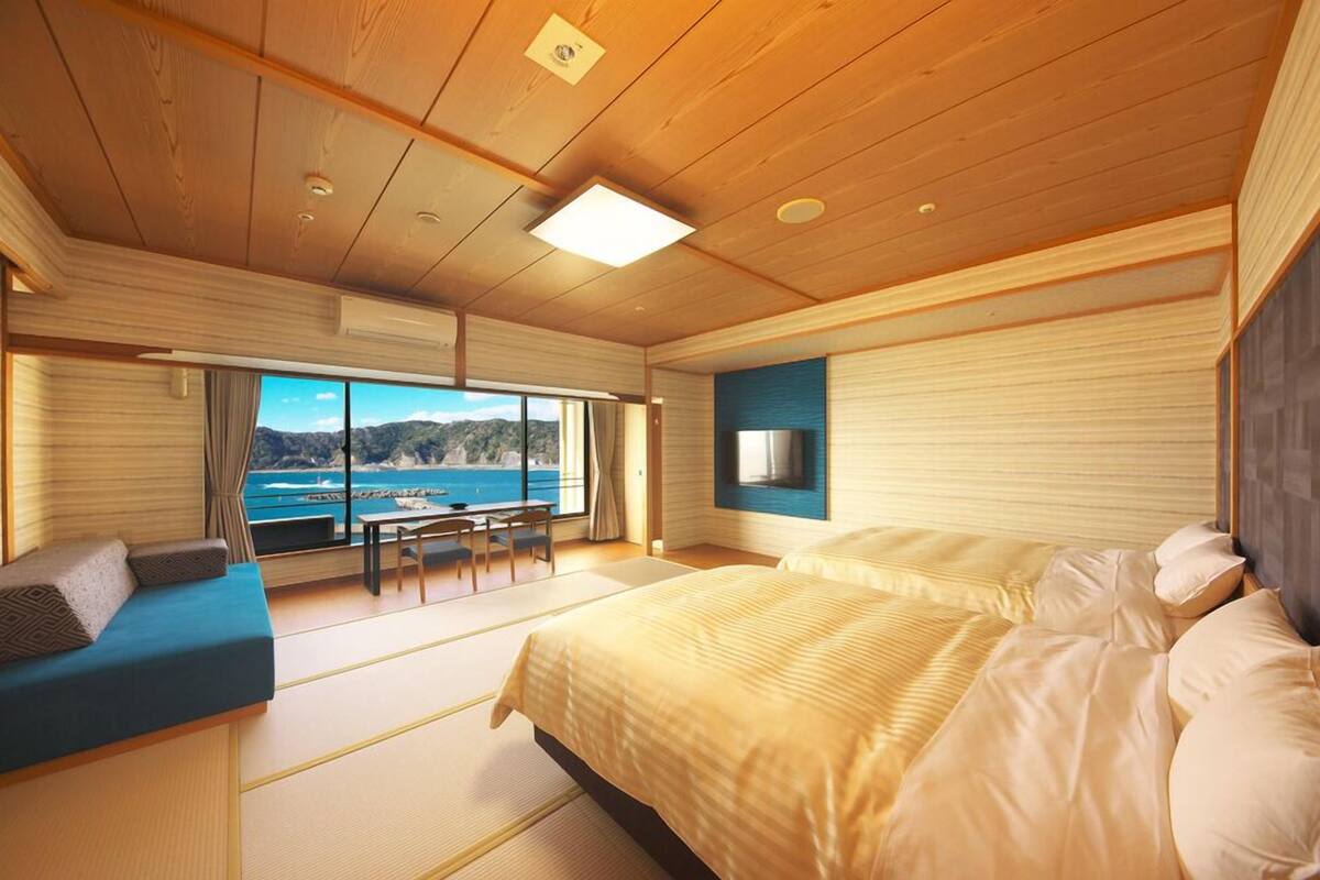 A room with a bed, a seating area, a table, and a view of the sea.