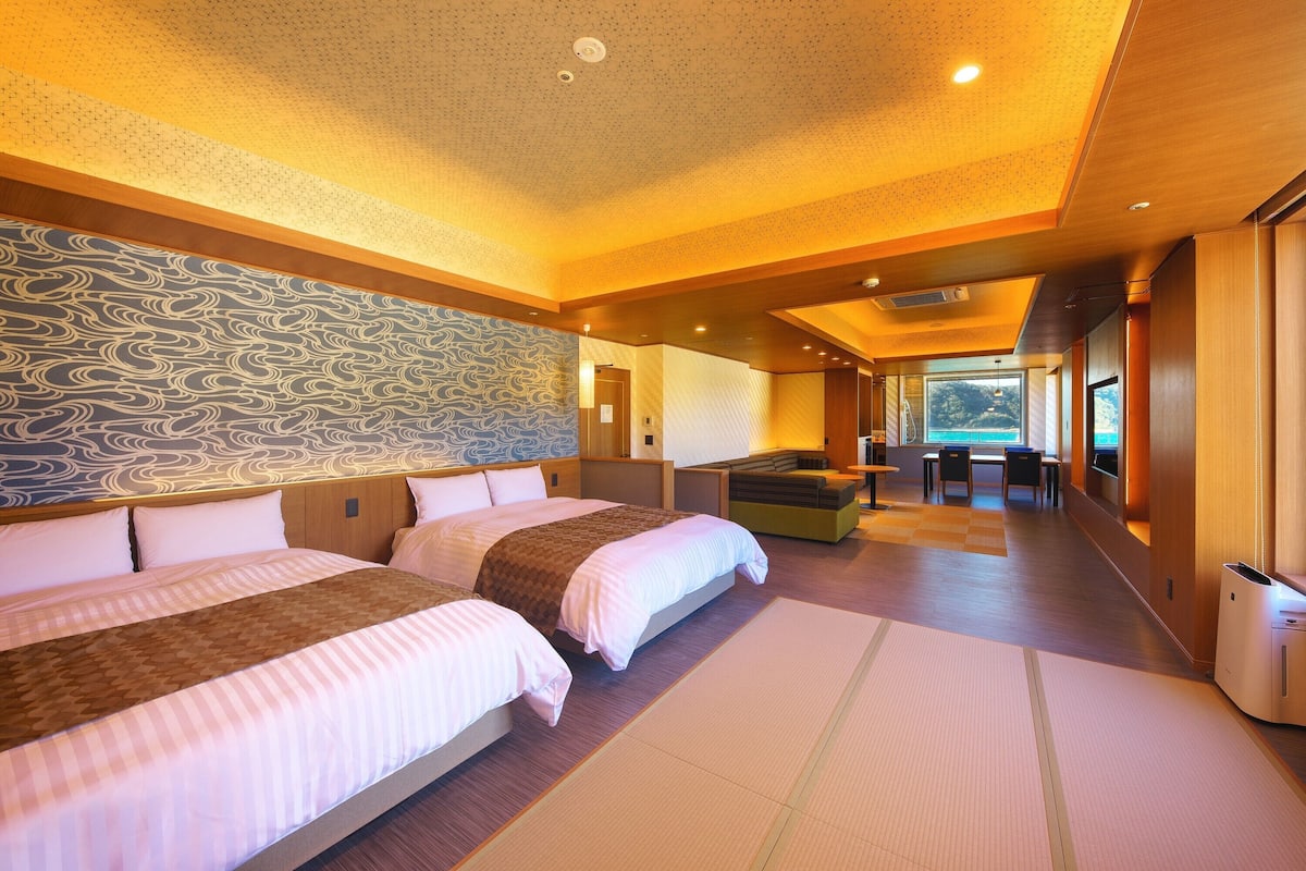 A hotel room with two beds, a large window, and a view of the sea.