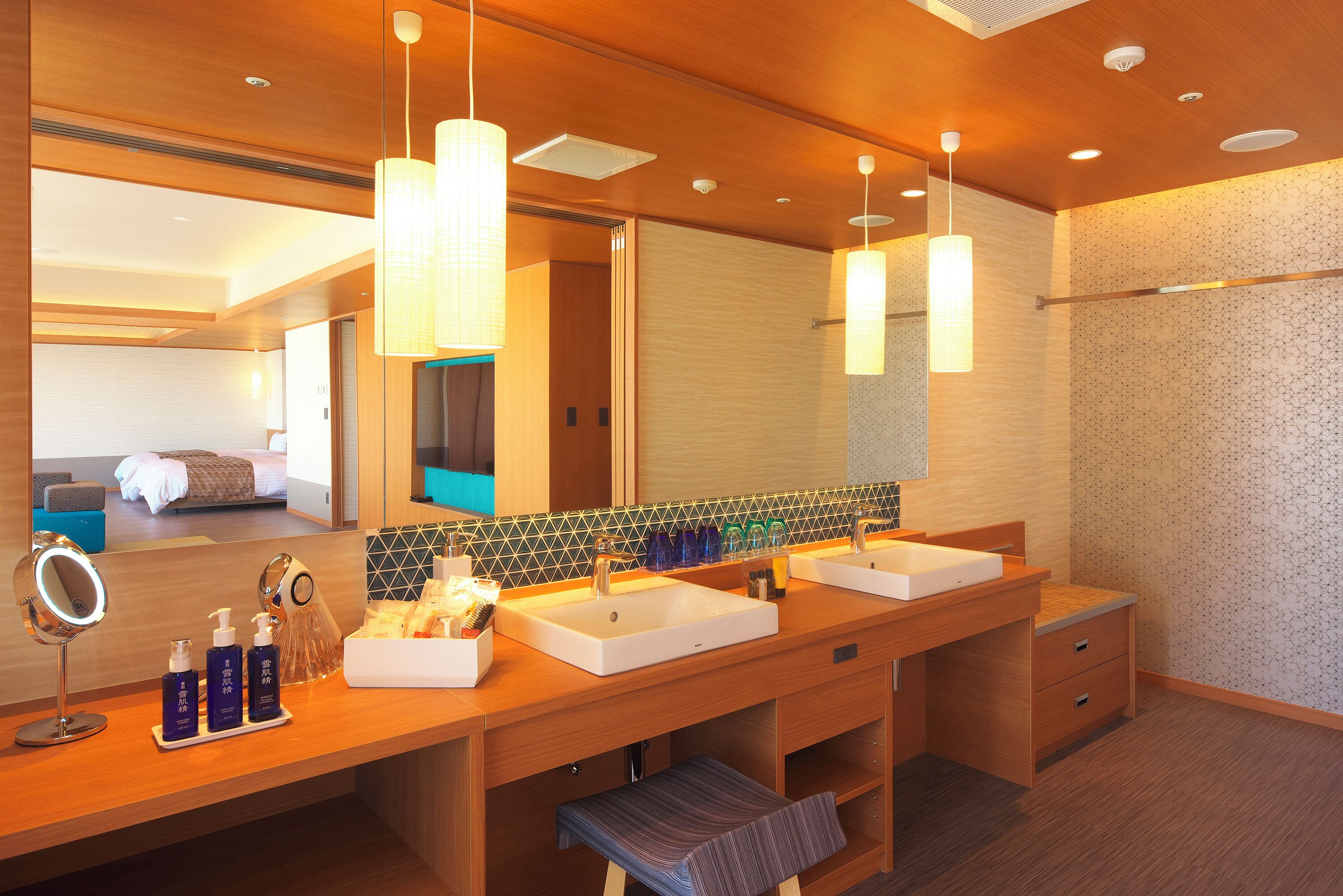 A hotel bathroom with two sinks, a large mirror, and a bench.
