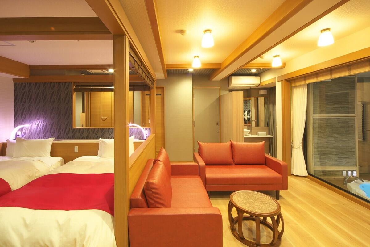 A hotel room with two beds, a sofa, a small round table, and a large window.