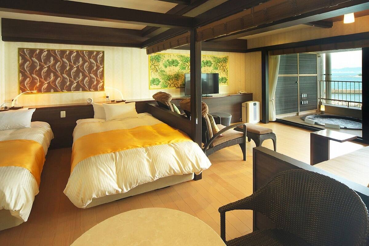 A hotel room with two beds, a sofa, a TV, a hot tub, and a balcony with a view.