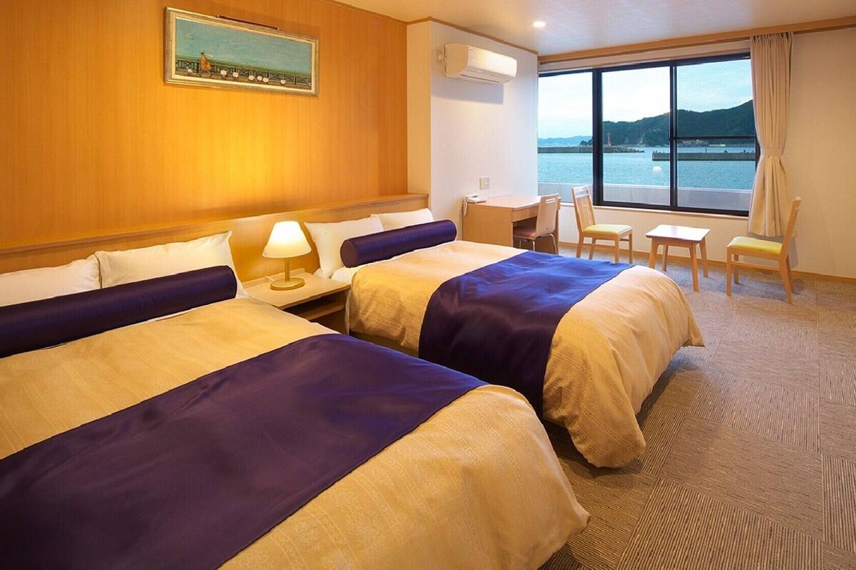 A hotel room with two beds, a desk, a chair, and a large window with a view of the water.