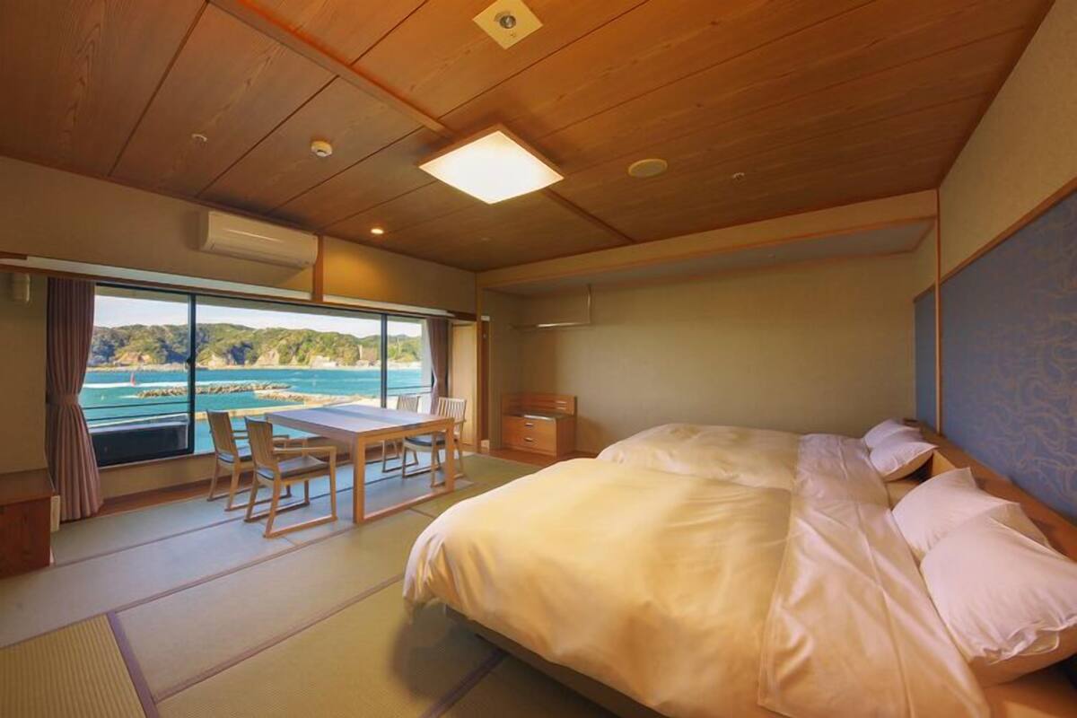 A bedroom with a large bed, a table, chairs, and a view of the sea.
