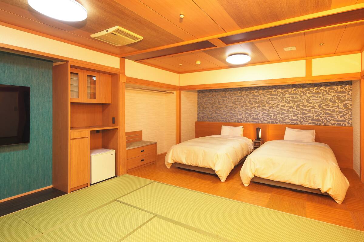 A hotel room with two beds, a small refrigerator, a television, and a wooden ceiling.