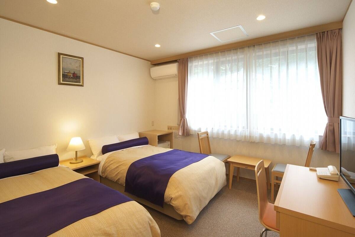 A hotel room with two beds, a desk, a chair, a television, and a window with curtains.
