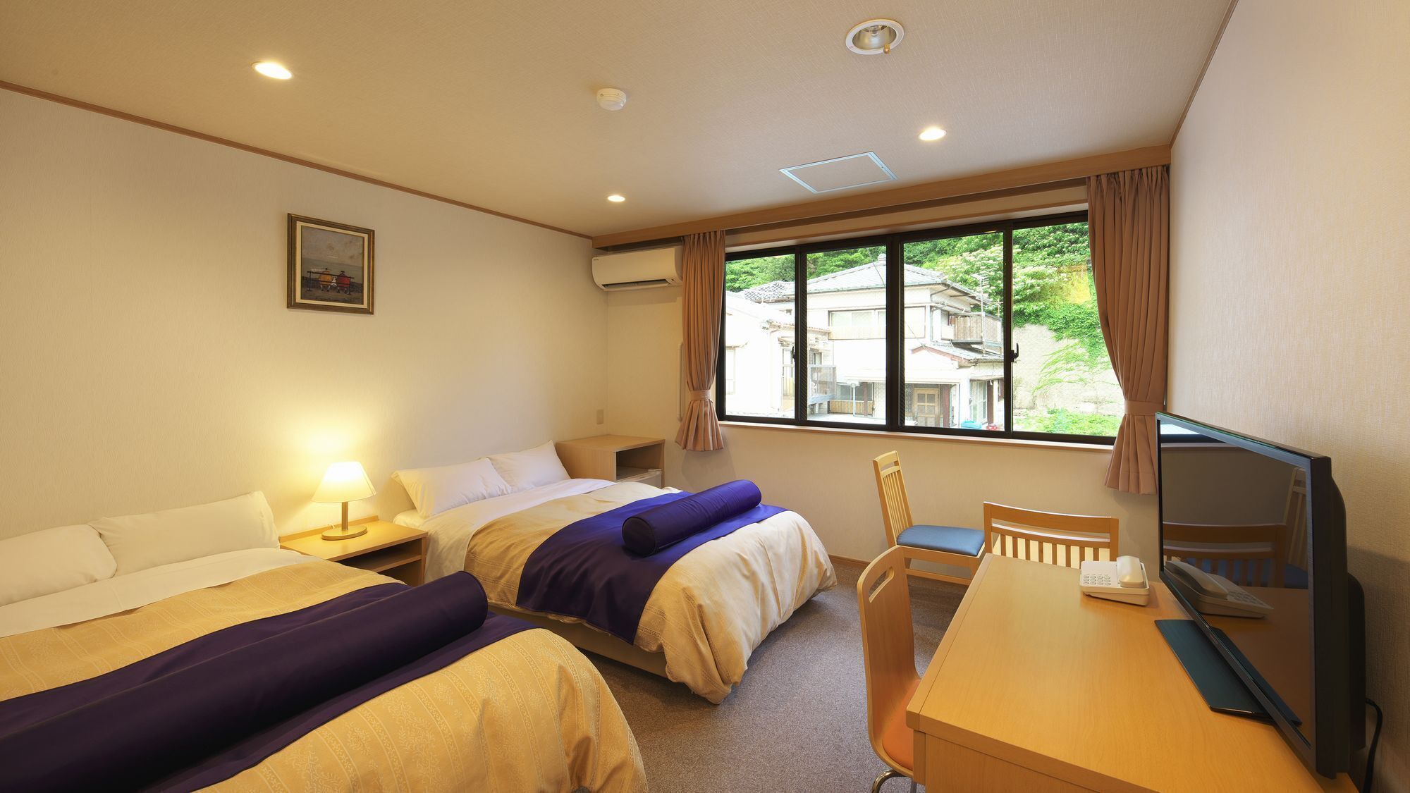 A hotel room with two beds, a desk with a computer, a chair, and a window with a view of buildings.