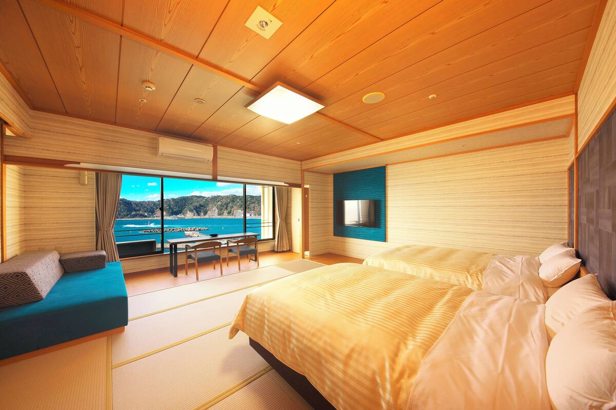 A room with a bed, a sofa, a table, and a view of the sea.