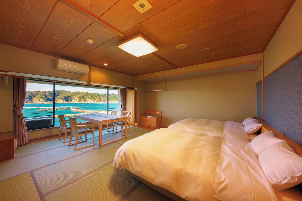 A room with a bed, a table, chairs, and a view of the sea.