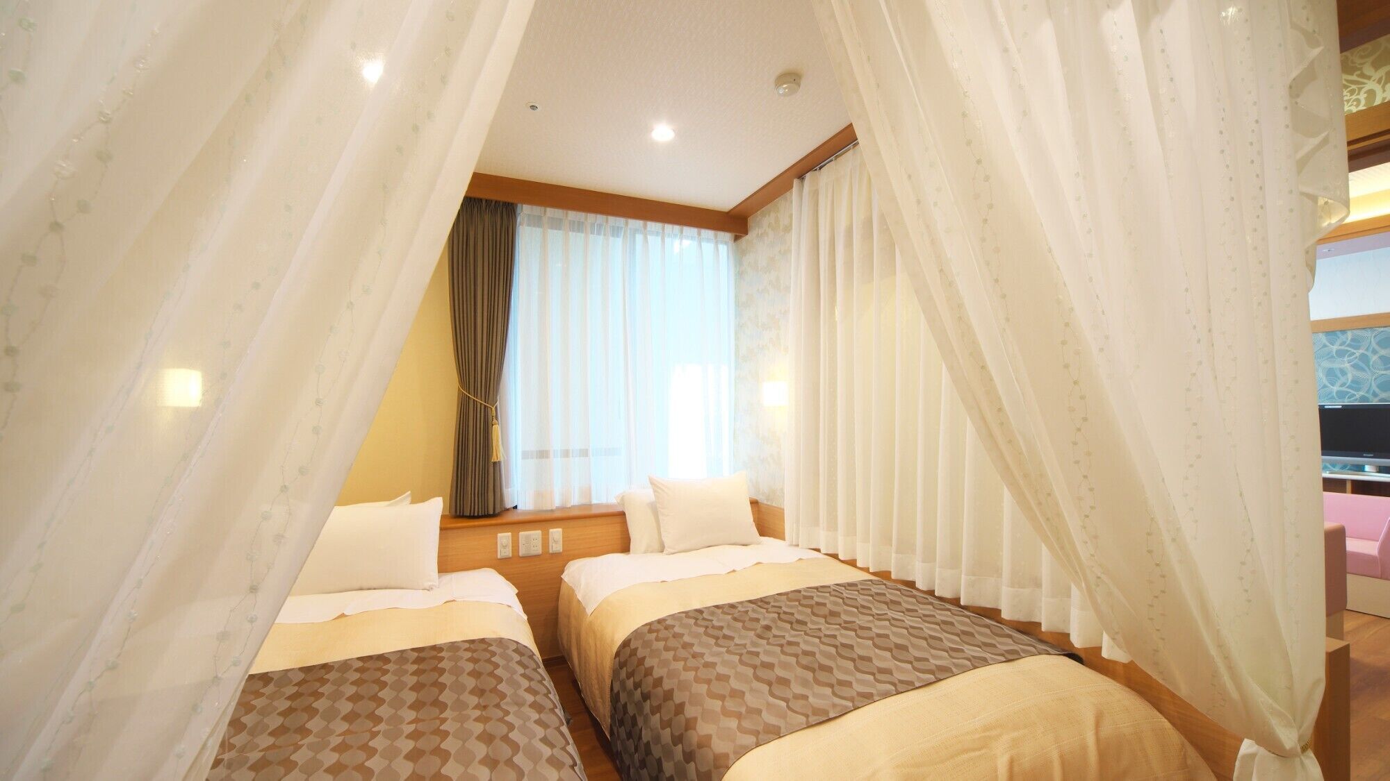 A hotel room with two beds, a window with curtains, and a television in the corner.