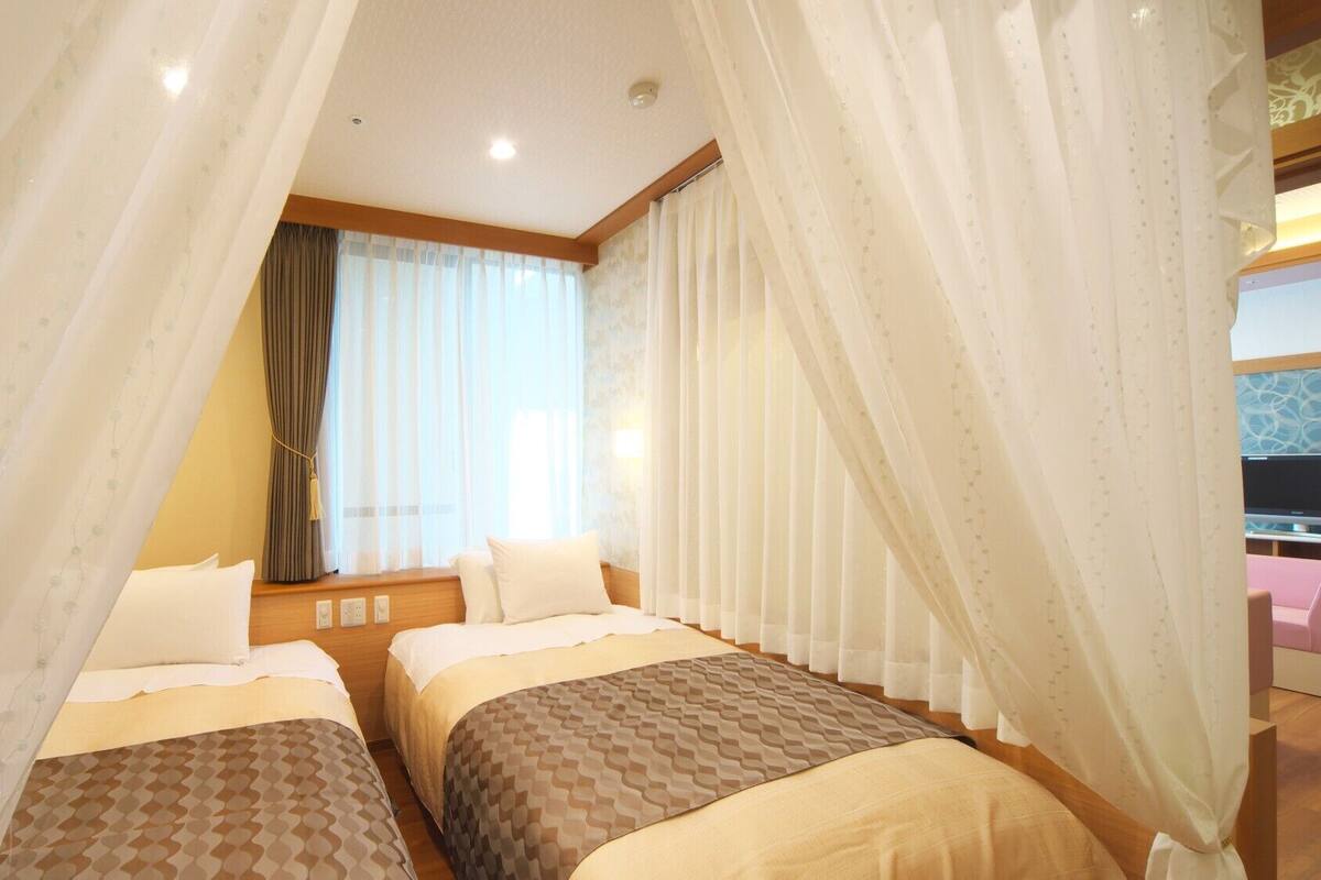 A hotel room with two beds, a window with curtains, and a television in the corner.