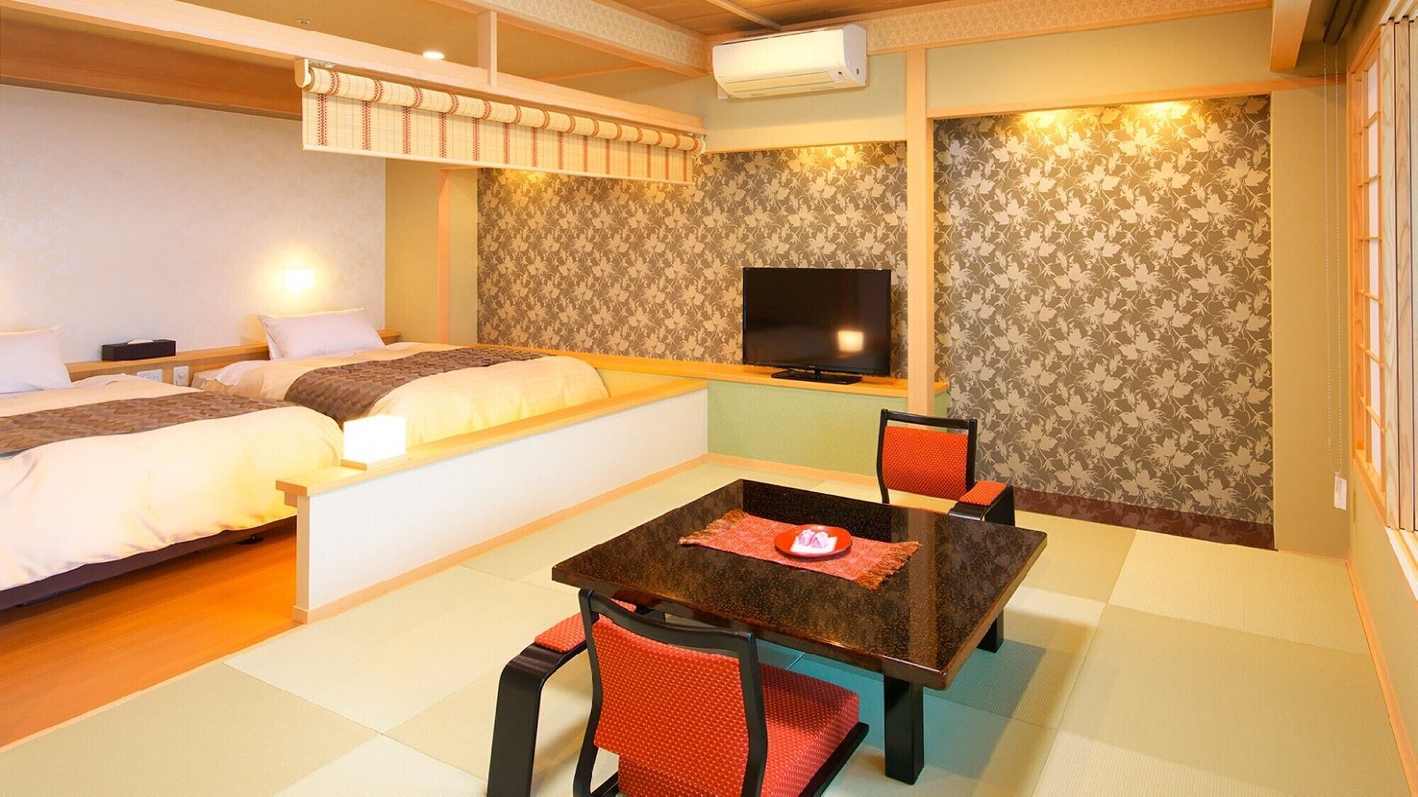 A hotel room with two beds, a TV, a table with chairs, and a patterned wall.