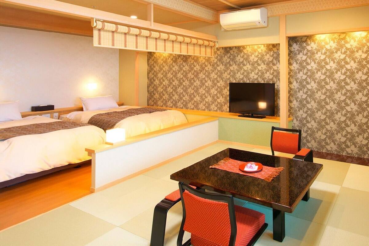 A hotel room with two beds, a TV, a table with chairs, and a patterned wall.