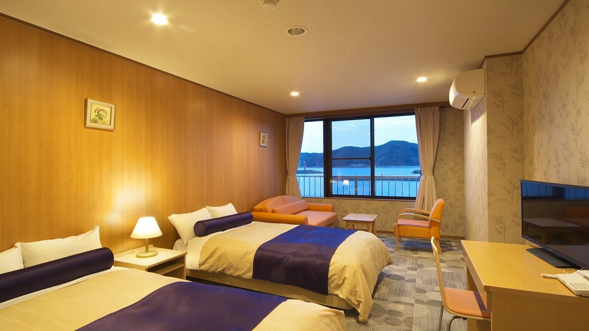 Camera d'albergo con due letti, una scrivania, una sedia, una televisione e un'ampia finestra vista mare.
