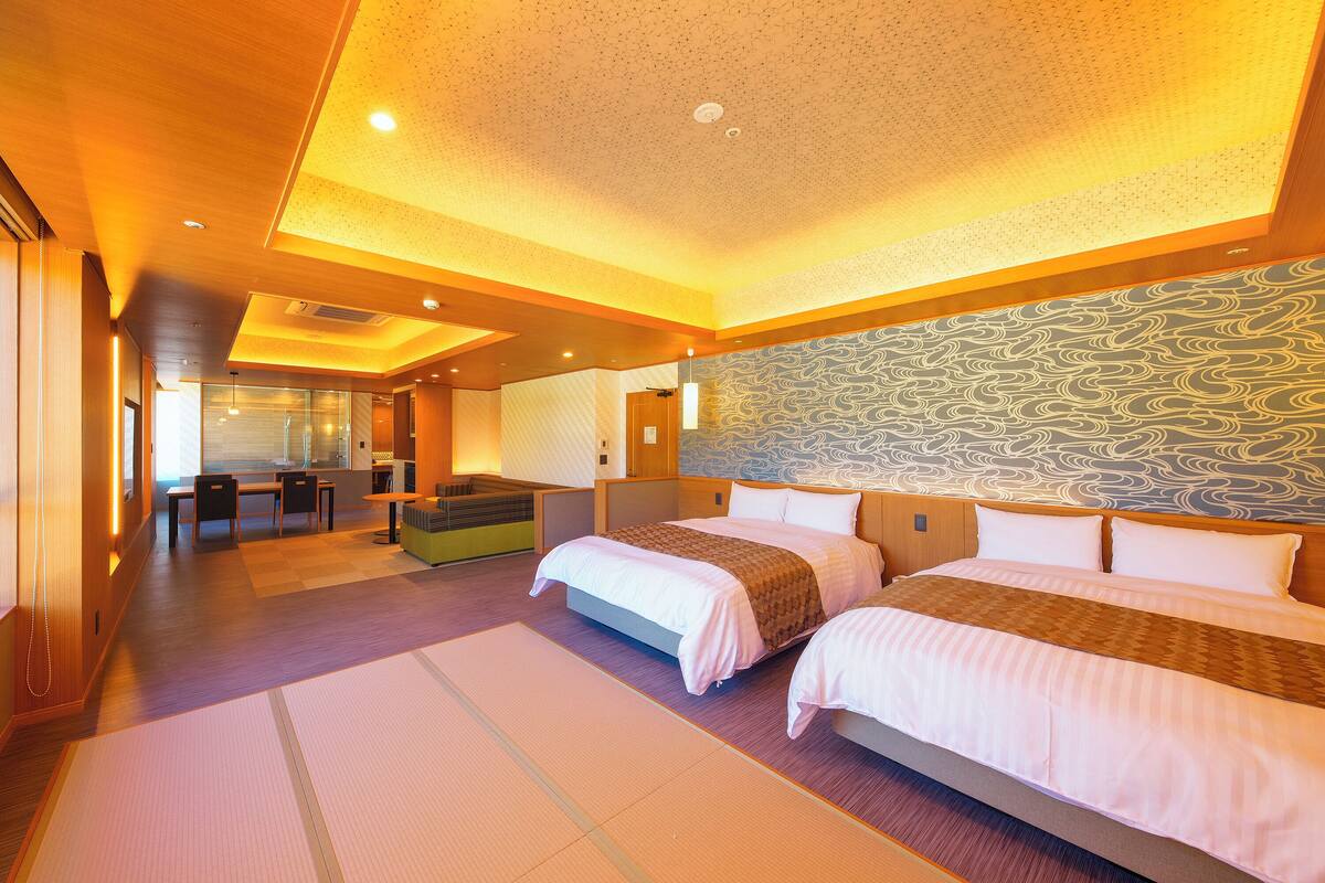 A hotel room with two beds, a dining area, and a view of the city.
