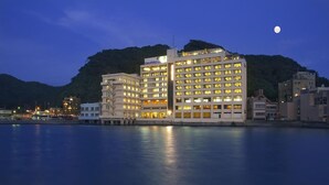 Ett hotell med flera våningar och många fönster, beläget vid en sjö eller ett annat vattendrag med ett berg i bakgrunden.