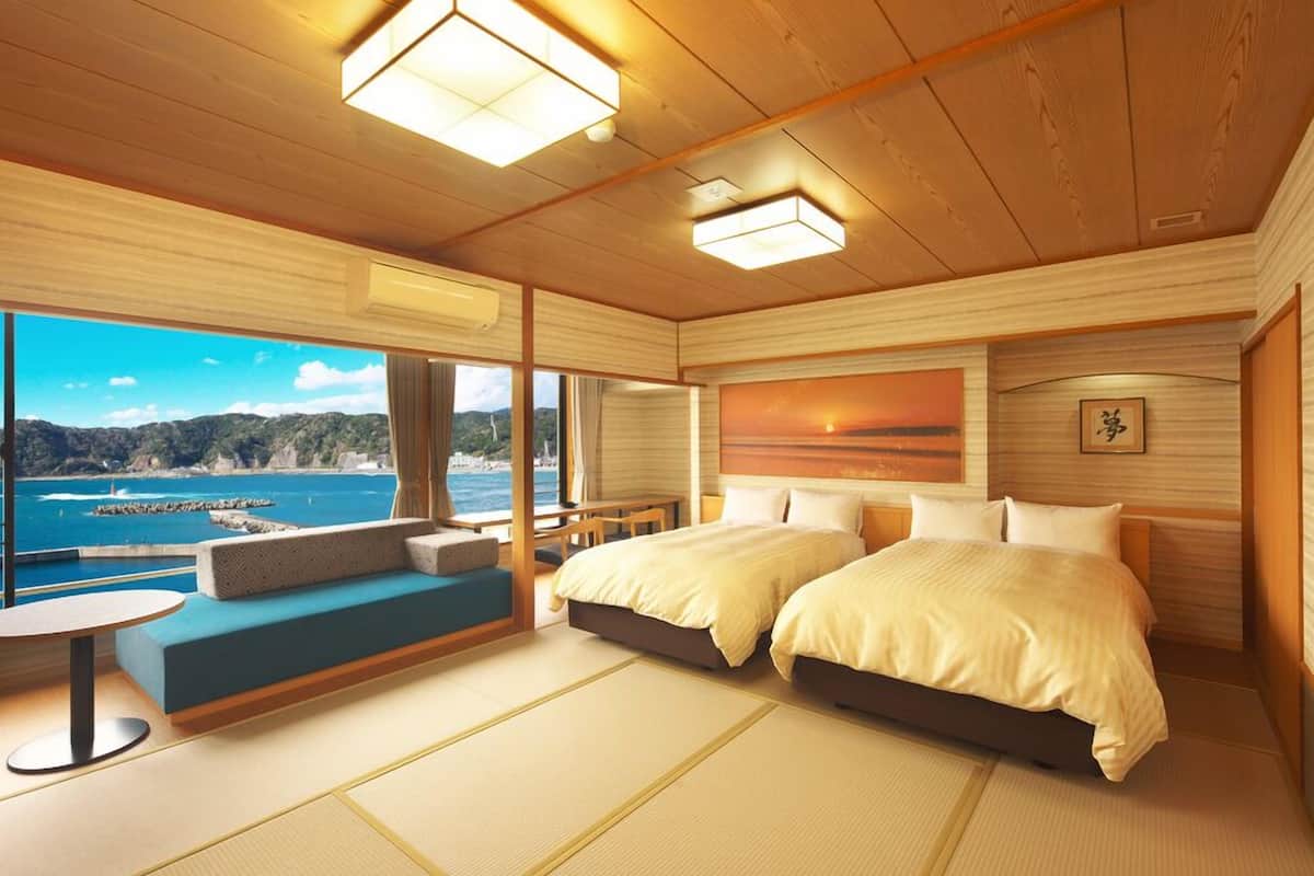 A room with two beds, a sofa, a table, and a view of the sea.