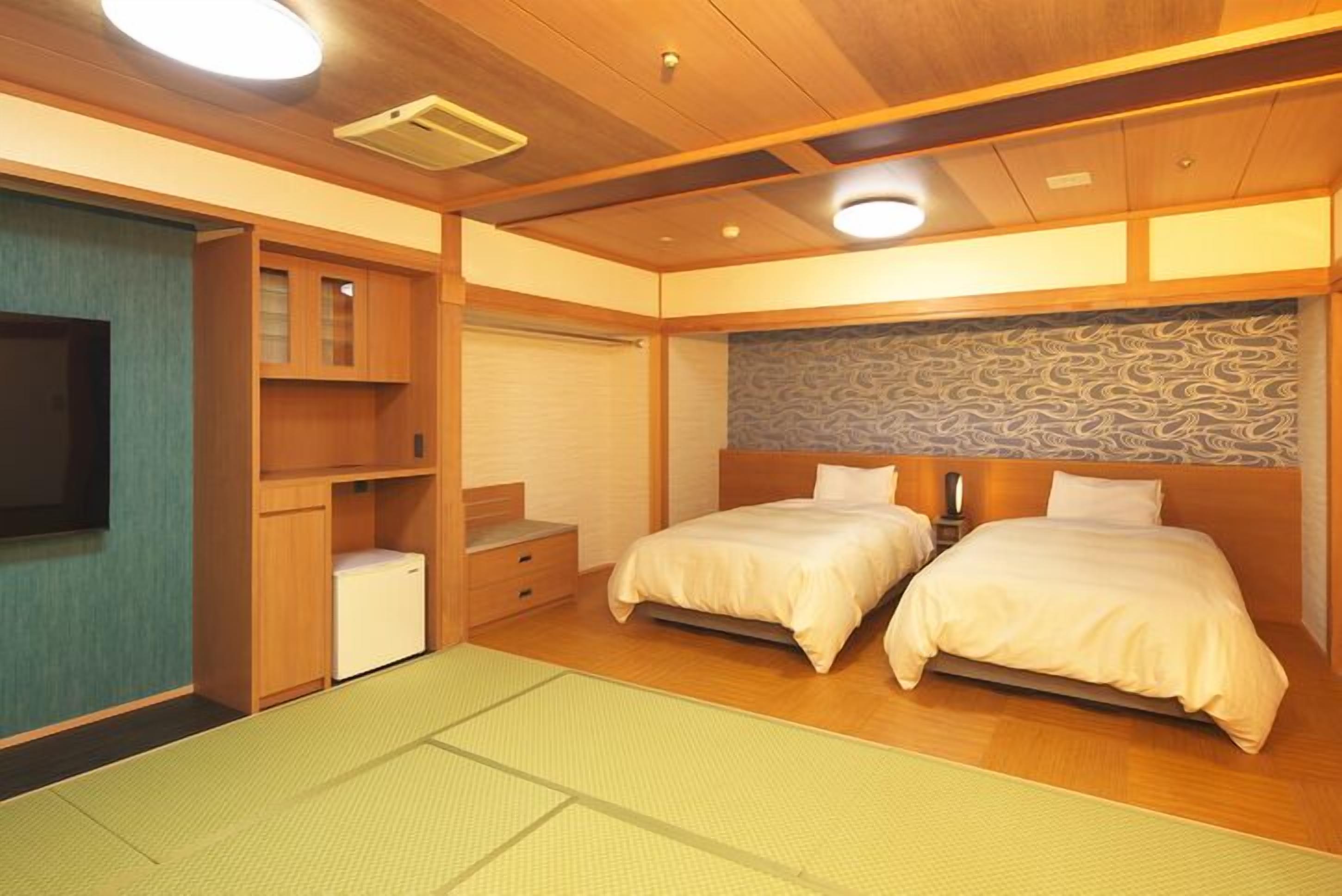 A room with two beds, a small desk, a television, and a patterned wall.