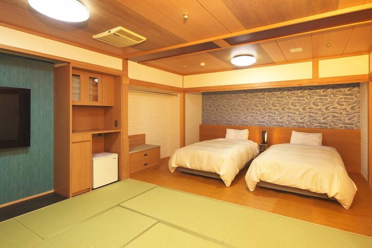 A room with two beds, a small desk, a television, and a patterned wall.