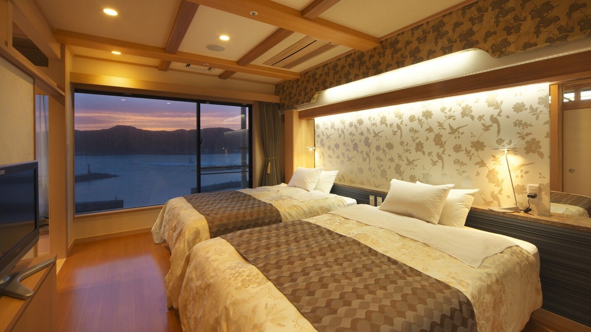A hotel room with two beds, a large window with a view of a body of water, and a wooden ceiling.