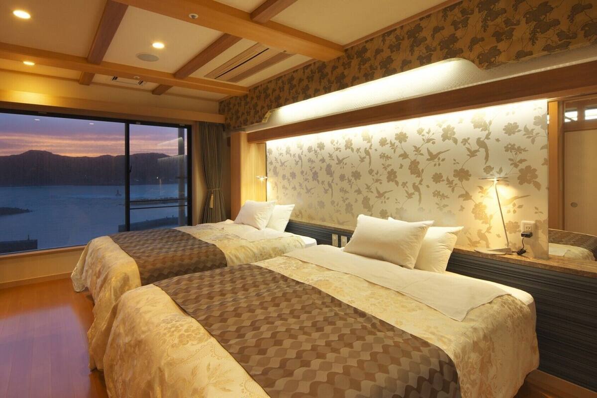 A hotel room with two beds, a large window with a view of a body of water, and a wooden ceiling.