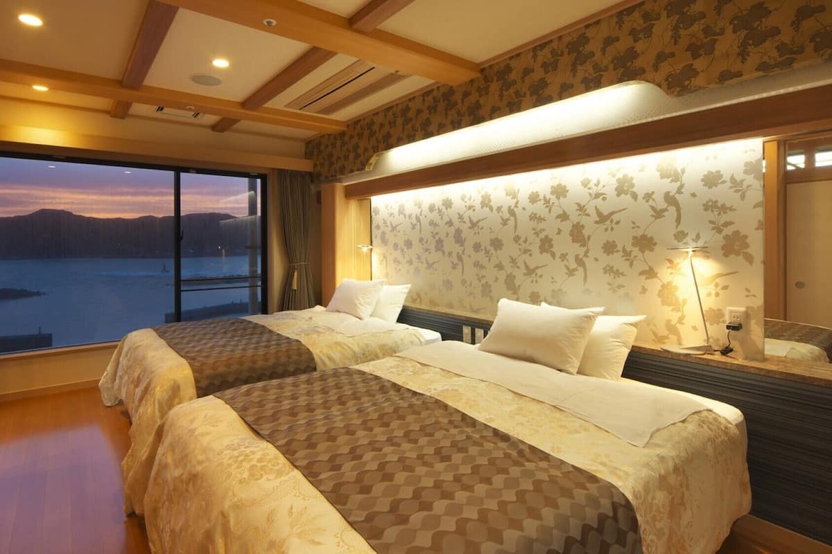 Ein Hotelzimmer mit zwei Betten, einem großen Fenster mit Blick auf ein Gewässer und einer Holzbalkendecke.