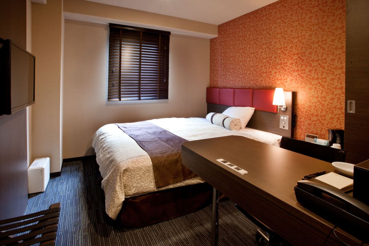 Una habitación de hotel con cama, escritorio, lámpara y televisor.
