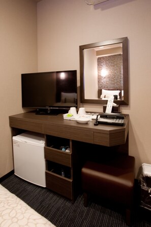 A hotel room with a flat-screen TV, a desk with a telephone, a small refrigerator, a mirror, and a bed.