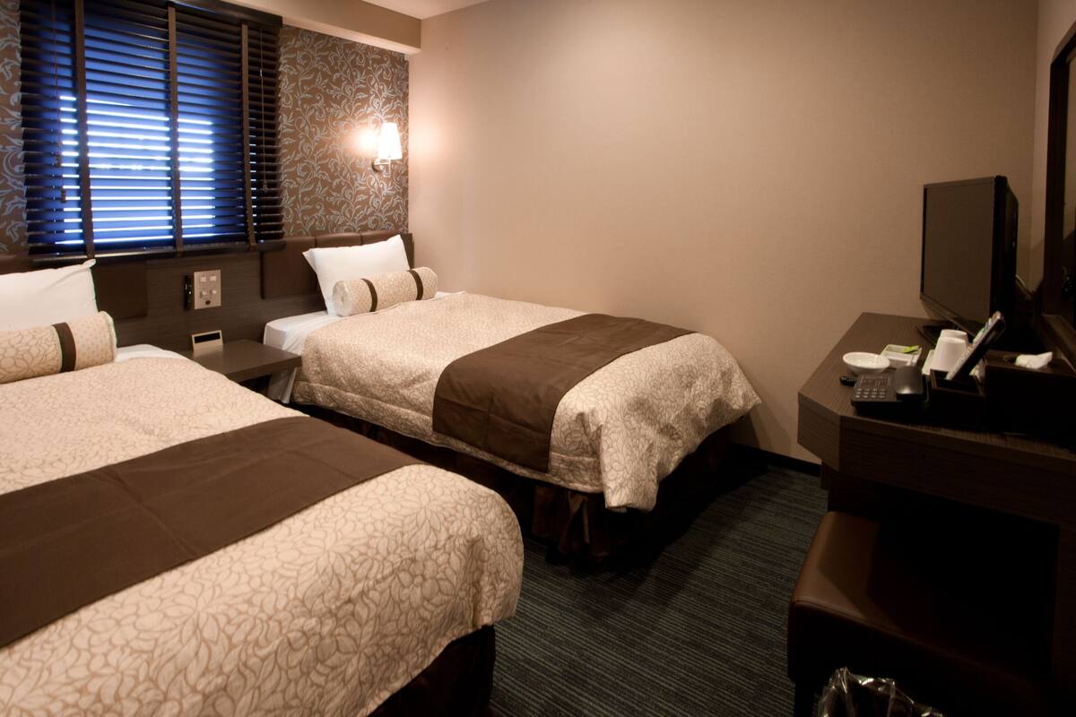 Habitación de hotel con dos camas, un escritorio con ordenador y una televisión.