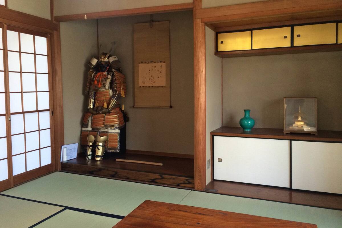 A traditional Japanese room with tatami flooring, a shoji screen door, a wooden cabinet, and a display of samurai armor.