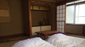 Una habitación japonesa tradicional con suelo de tatami, dos camas con ropa de cama blanca, una mesa de madera y un shoji.