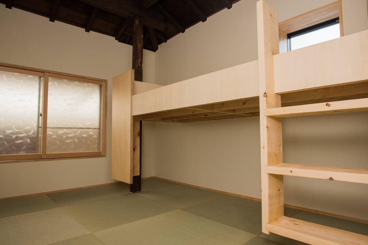 A room with a bunk bed, tatami mat flooring, a sliding door, and a window with frosted glass.