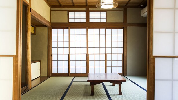 Una habitación japonesa tradicional con suelo de tatami, una mesa de madera, puertas correderas y un ventilador de techo.