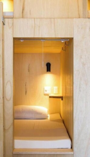 Ett litet, avskilt rum med träpanel, en säng, en liten hylla med två föremål och en väggmonterad lampa.