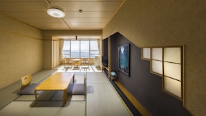 A traditional Japanese room with tatami flooring, a low wooden table, and a large window offering a city view.